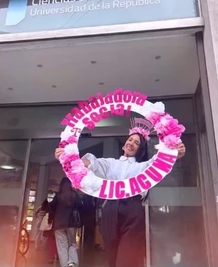 Recién recibida en la puerta de la facultad con un aro de flores rosadas que dice Trabajadora Social, Lic. Acuña