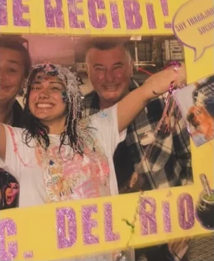 Festejo de recibimiento con un cartel amarillo con letras violetas con glitter que dice Me recibí, Lic. del Río