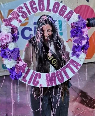 Recién recibida llena de serpentina con un aro de flores violetas que dice Psicóloga, Lic. Motta