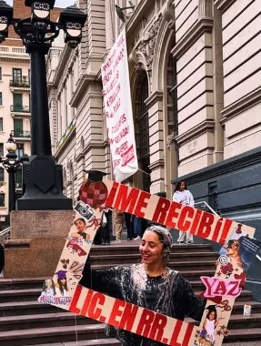 Recién recibida en una escalinata con un cartel rojo lleno de fotos que dice Me recibí, Lic. en RR.II